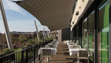 An outdoor dining area with tables and chairs, a wooden deck, and a large canopy providing shade.