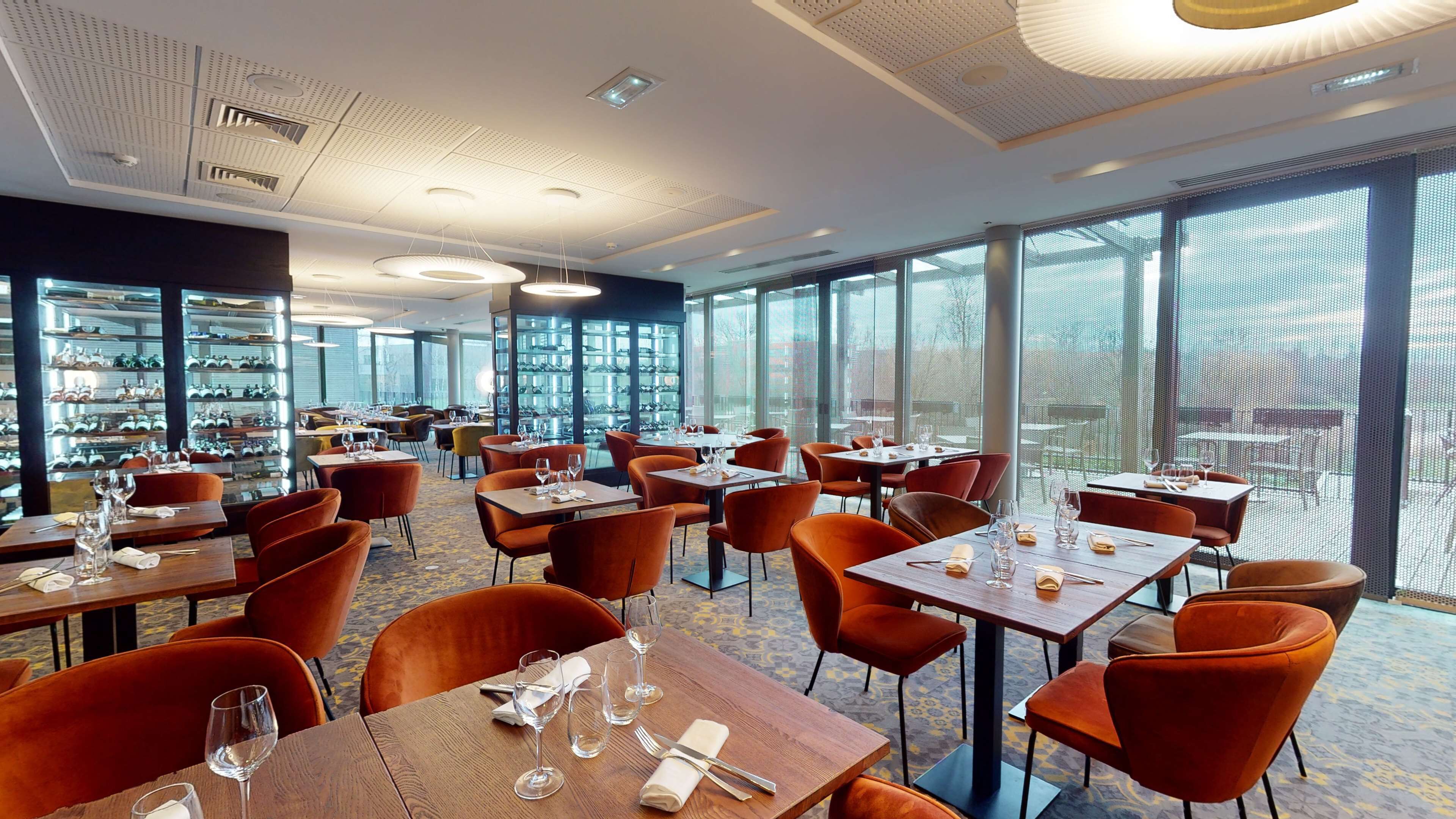 Ein Restaurant mit Tischen, Stühlen, großen Fenstern und einer Decke mit Lampen.