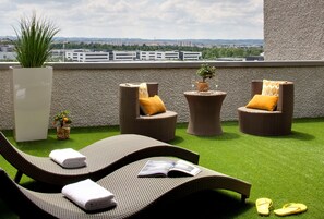 A rooftop lounge area with wicker chairs, a small table with a plant, and a view of the cityscape. - DoubleTree by Hilton Lyon Eurexpo & Spa (Saint-Priest)
