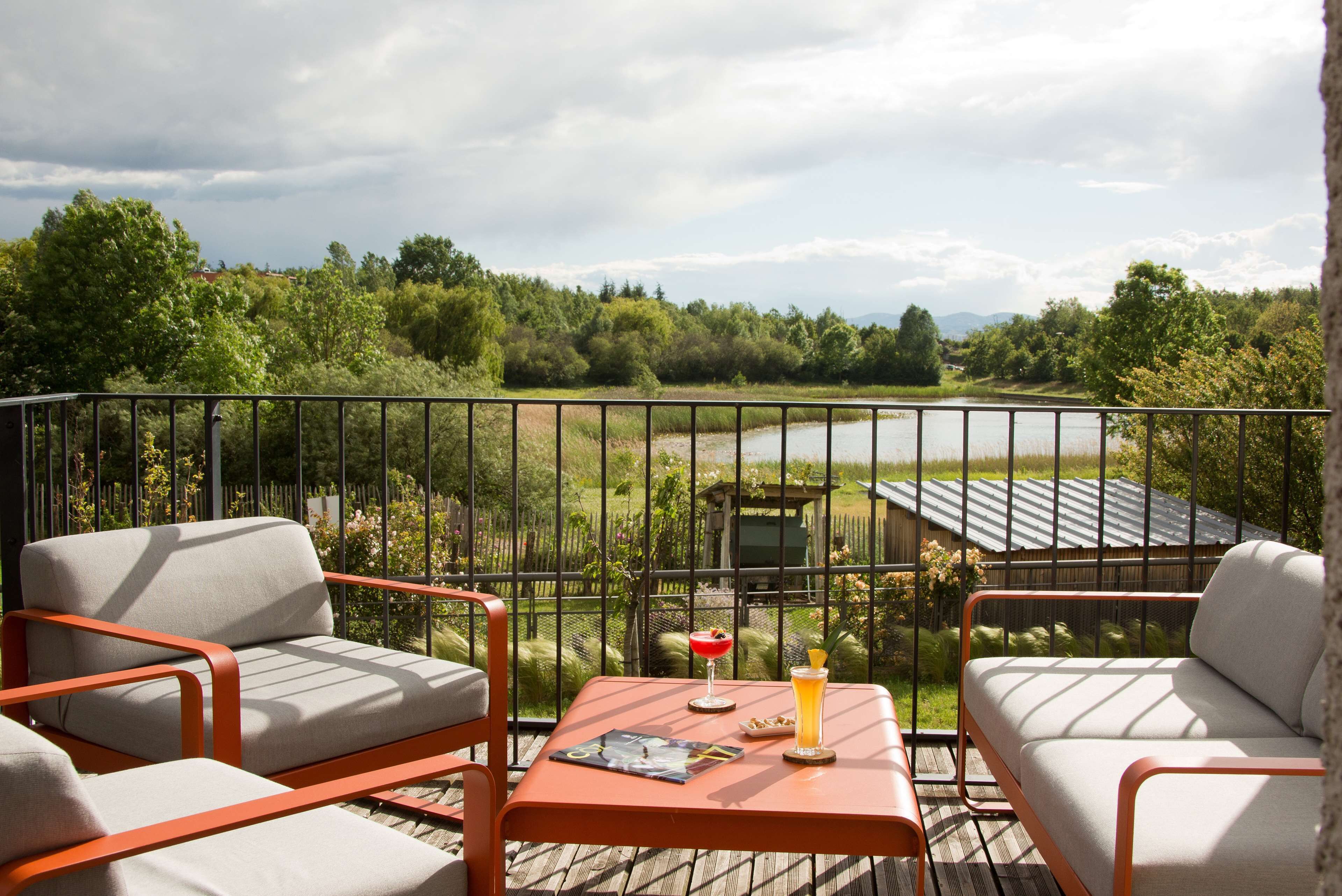 A balcony with two chairs and a table, overlooking a garden and a house.