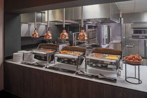 A buffet setup with various food stations, stainless steel appliances, and copper pendant lights. - DoubleTree by Hilton Lyon Eurexpo & Spa (Saint-Priest)