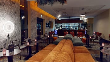 A modern bar area with a long sofa, multiple tables, and chairs.