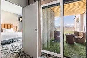 A hotel room with a bed, a large window, and a view of an outdoor area with a table and chairs. - DoubleTree by Hilton Lyon Eurexpo & Spa (Saint-Priest)