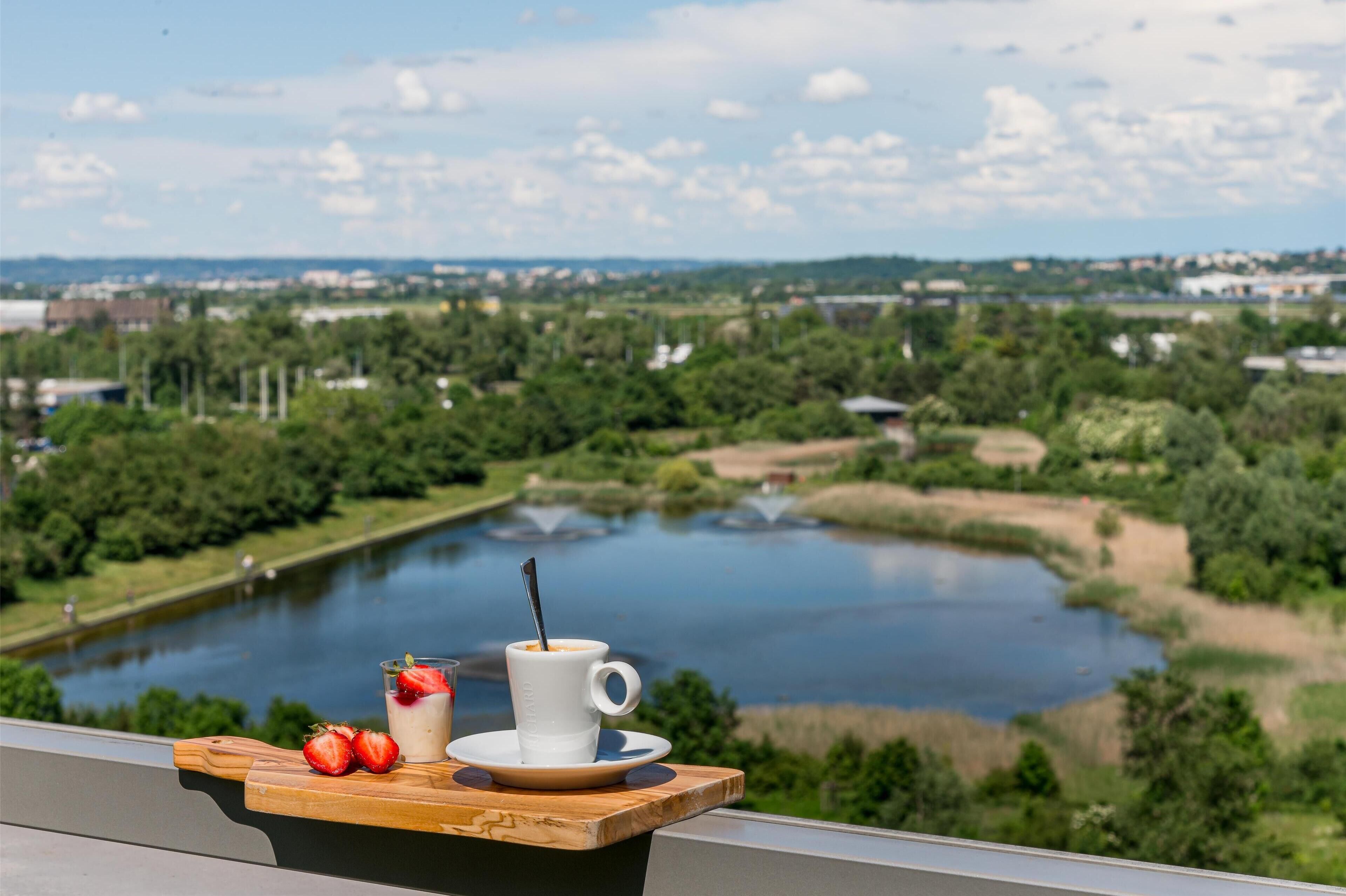 A scenic view of a river with a wooden table holding a cup of coffee and strawberries.