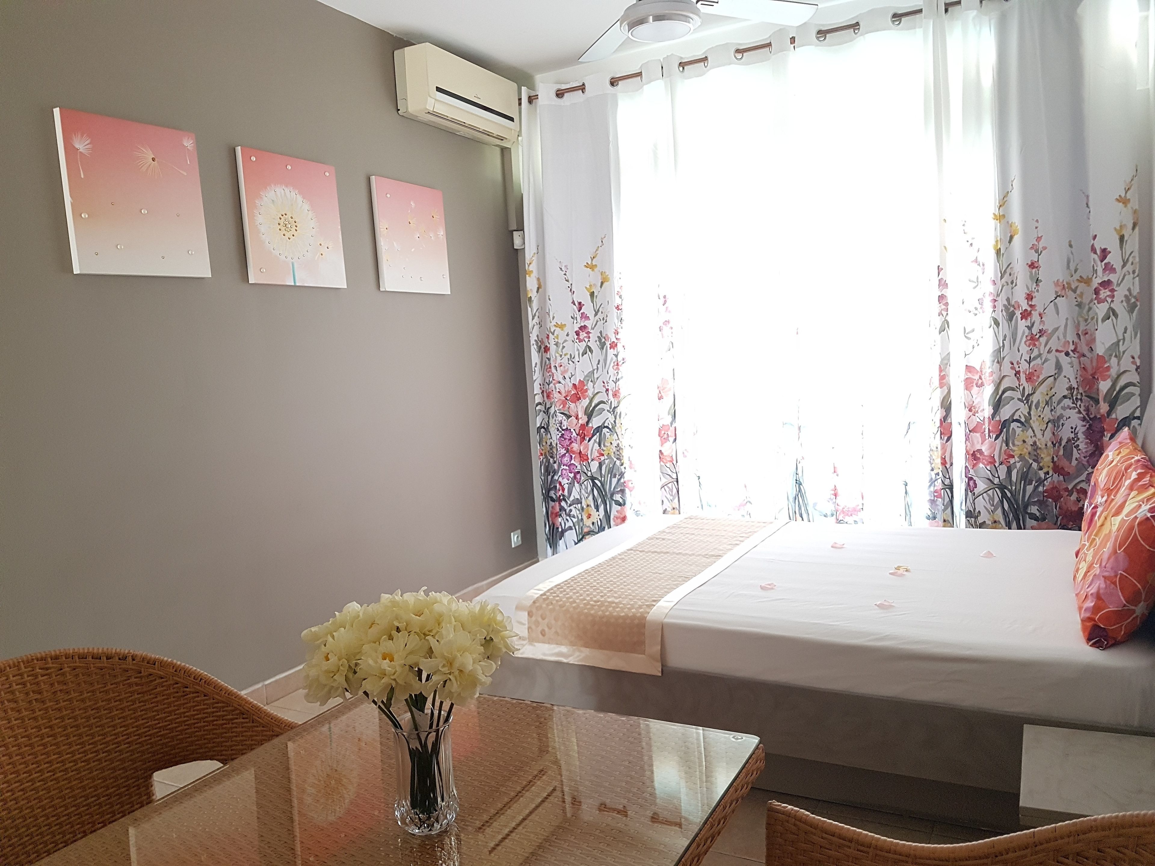 A room with a bed, a table with a vase of flowers, and wall art.