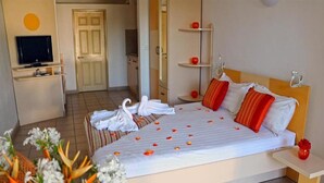 Quarto de hotel com cama, televisão, banheiro e área de refeições.