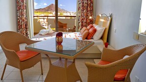 Uma varanda com cadeiras de vime, uma mesa de vidro e uma cama com almofadas.