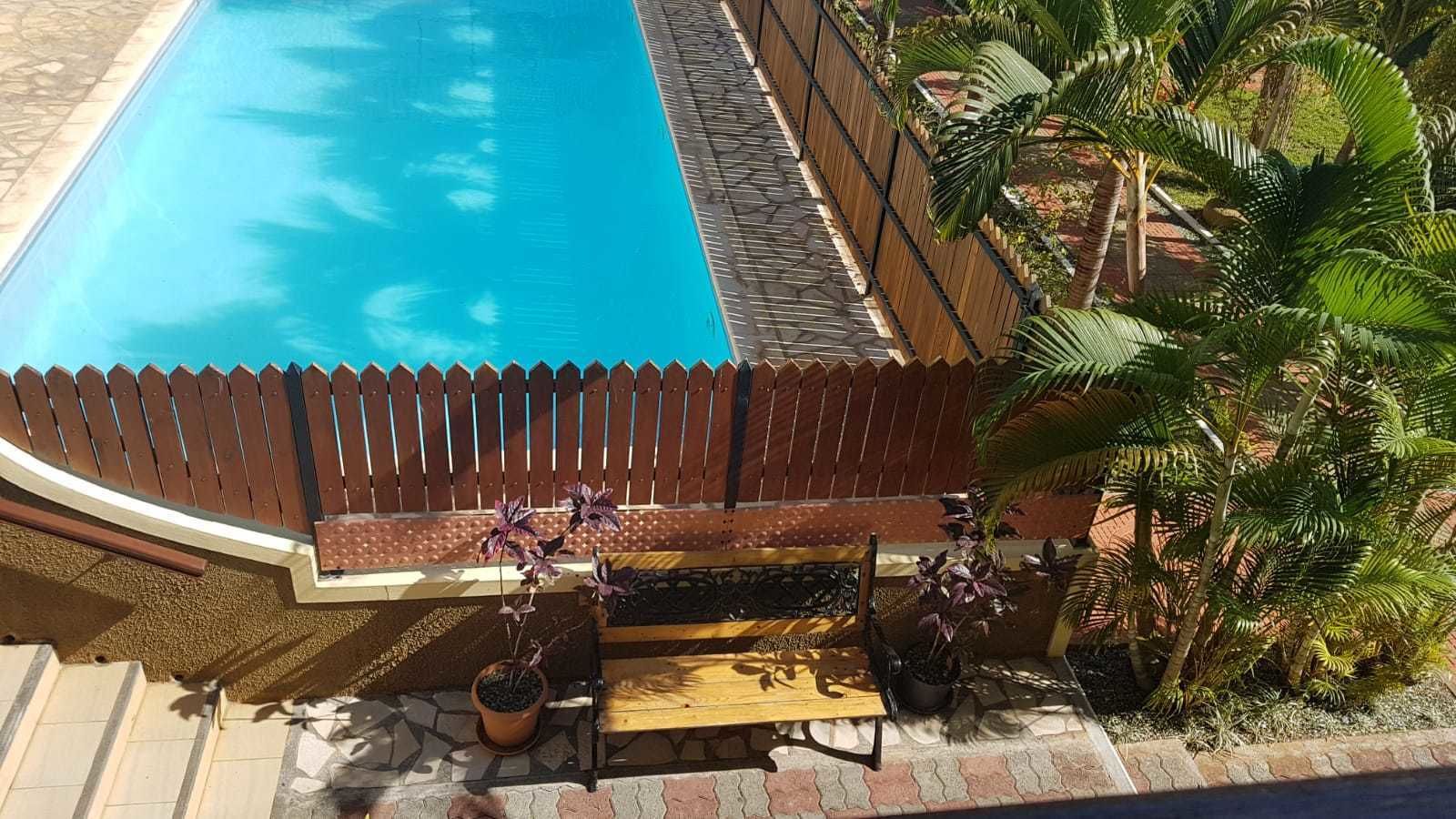 A swimming pool with a wooden fence, potted plants, and a bench.