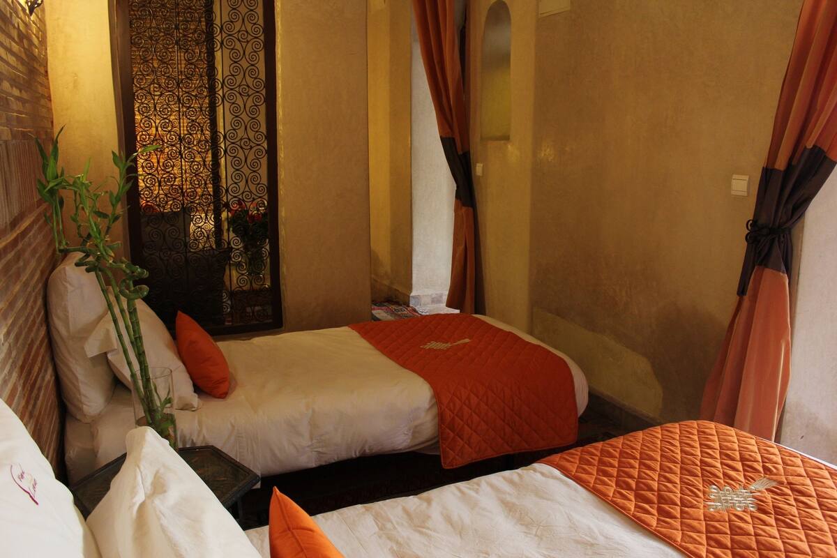 Une chambre d’hôtel avec deux lits, une petite table et un rideau décoratif.