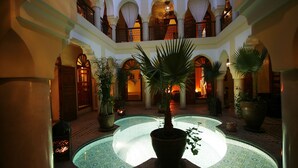 Ein weitläufiger Innenhof mit einem zentralen Brunnen, umgeben von Bögen und Blumentöpfen.