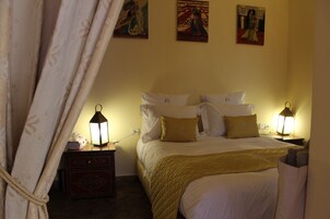 Una habitación de hotel con cama, mesitas de noche, lámpara y una obra de arte en la pared.