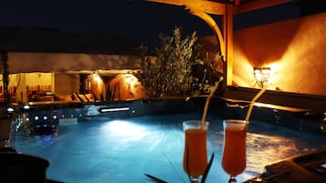A hot tub with two glasses of orange beverage, surrounded by wooden pergolas and plants.