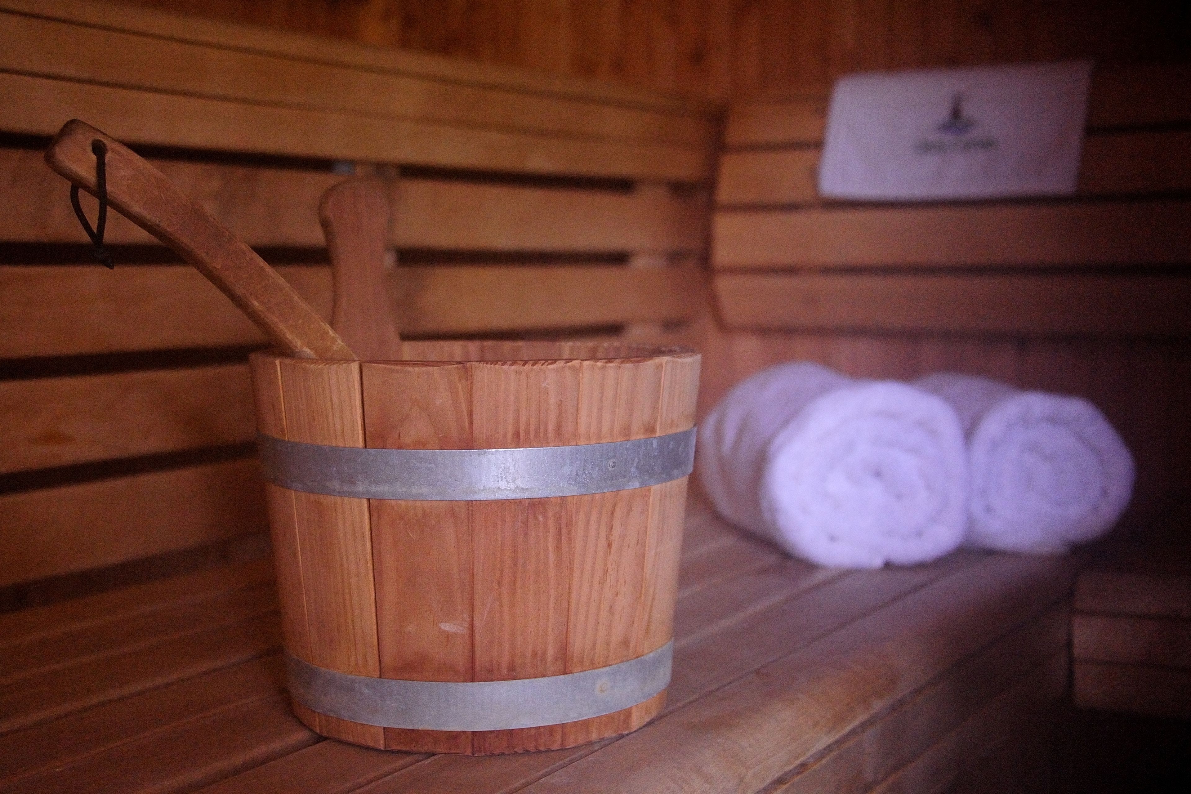 A wooden bucket with a handle, rolled towels, and a nameplate on a wooden bench.