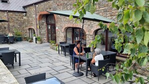 An outdoor patio area with stone flooring, outdoor seating, and a stone building in the background. - Llety Cynin (Carmarthen)