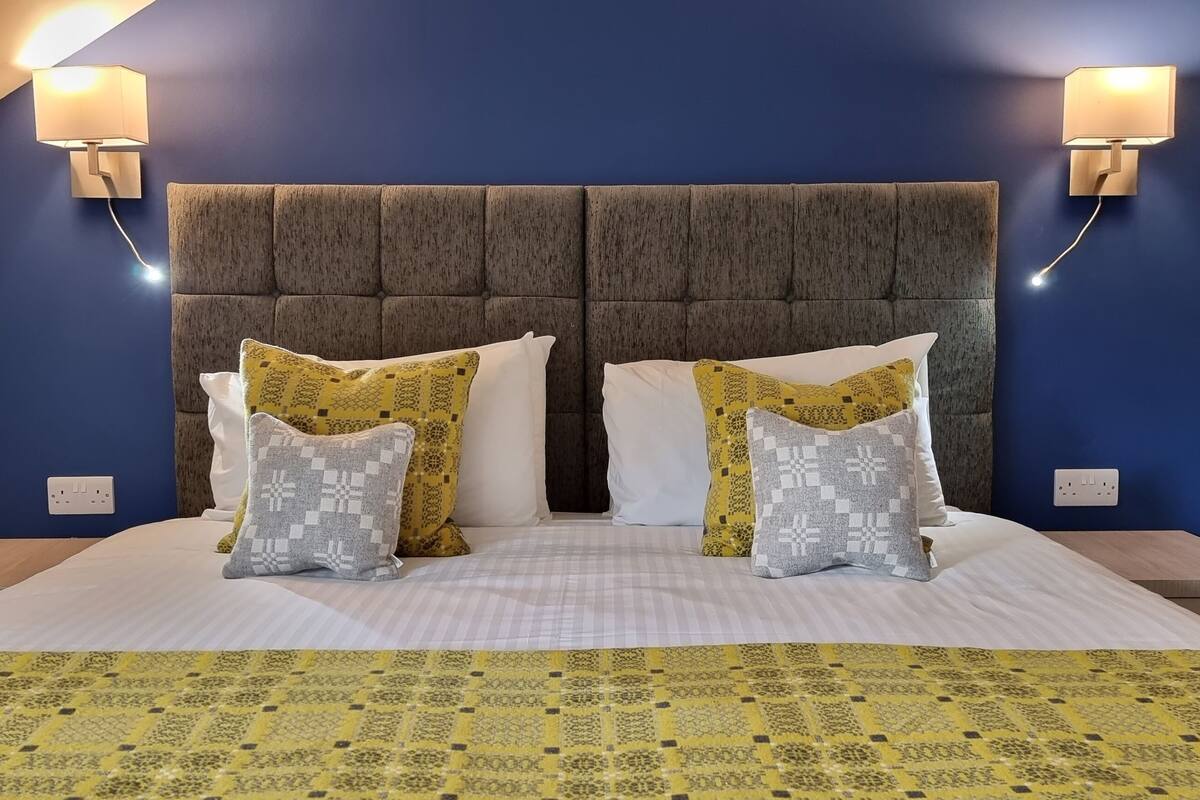 A bed with a patterned bedspread, two bedside tables, and a headboard with wall-mounted lights.