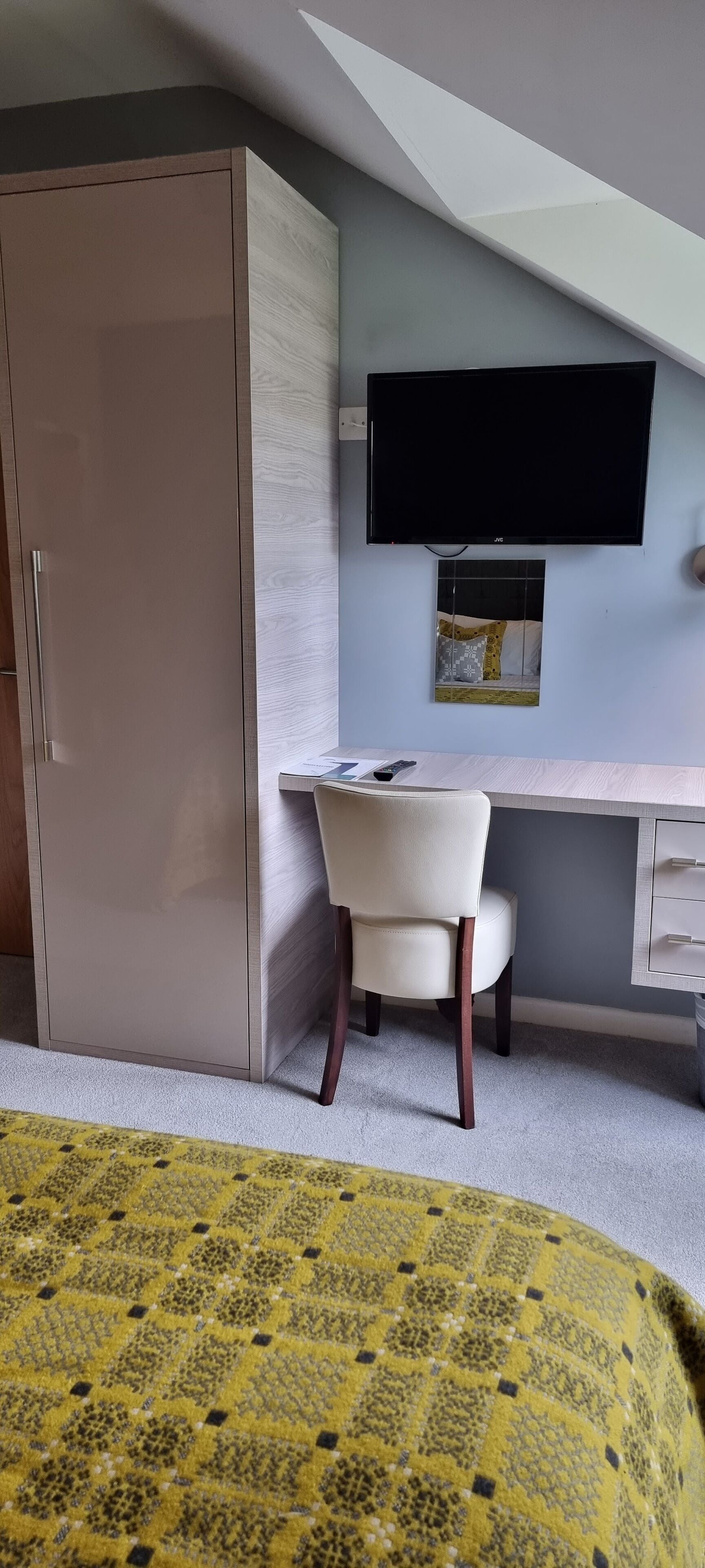 A bedroom with a bed, a desk, a chair, a wardrobe, and a TV on the wall.