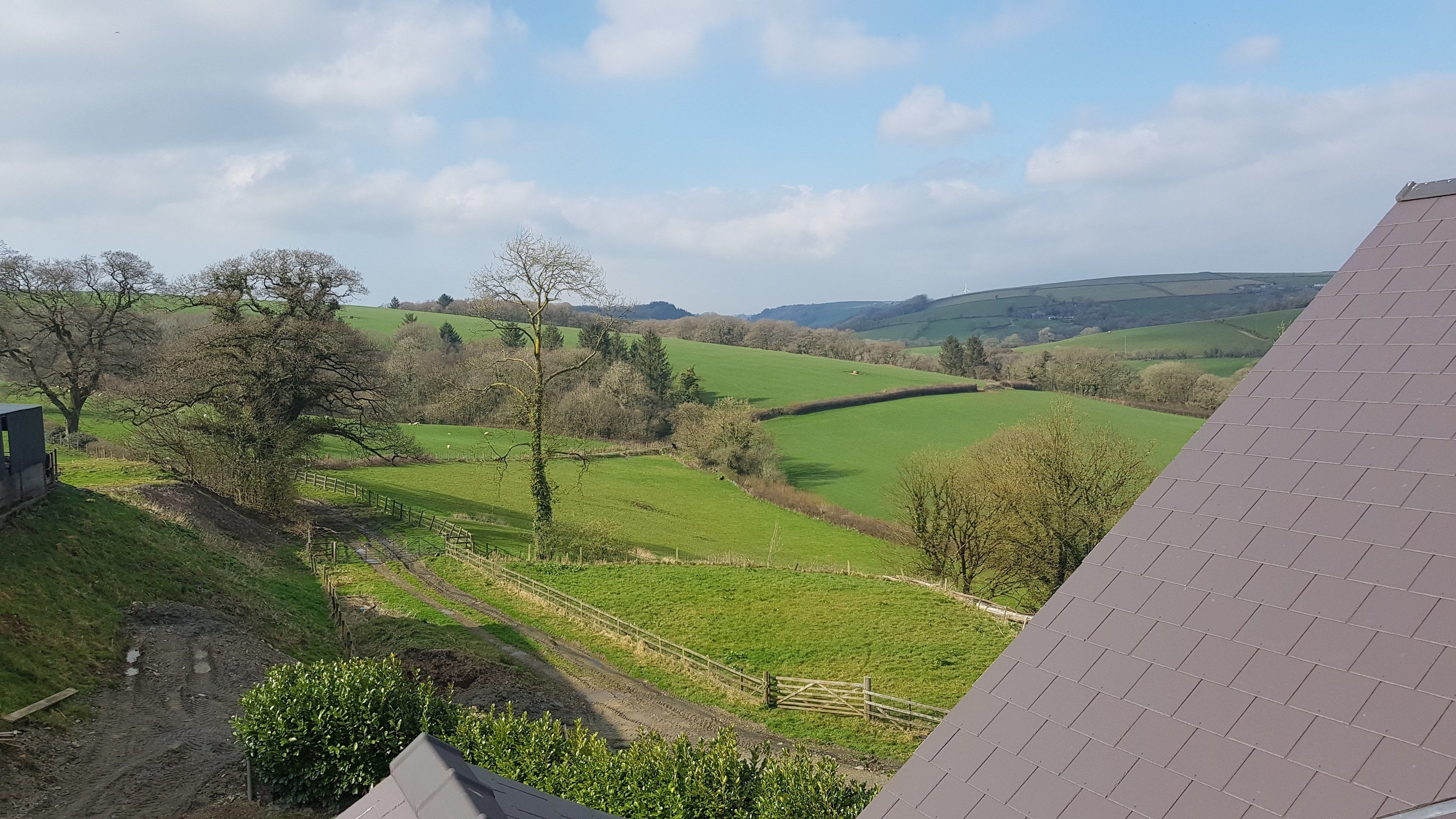 A rural landscape with rolling green fields, a wooden fence, and a clear sky.