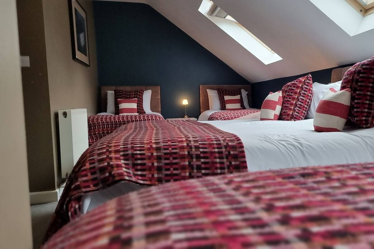 A hotel room with a sloped ceiling, two beds with checkered bedding, a headboard, and a skylight.