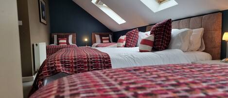 A hotel room with a sloped ceiling, two beds with checkered bedding, a headboard, and a skylight.