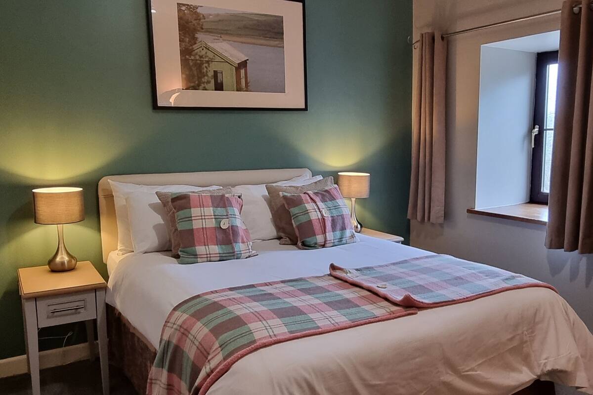 A neatly made bed with a plaid bedspread and pillows, a bedside lamp, and a framed picture on the wall.