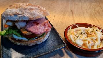 Un sándwich con lechuga, tomate y carne, junto con un plato de pasta con queso y pimiento.