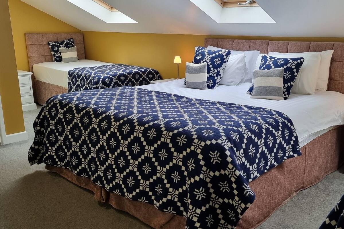 A bedroom with two beds, a skylight, and a nightstand with a lamp.