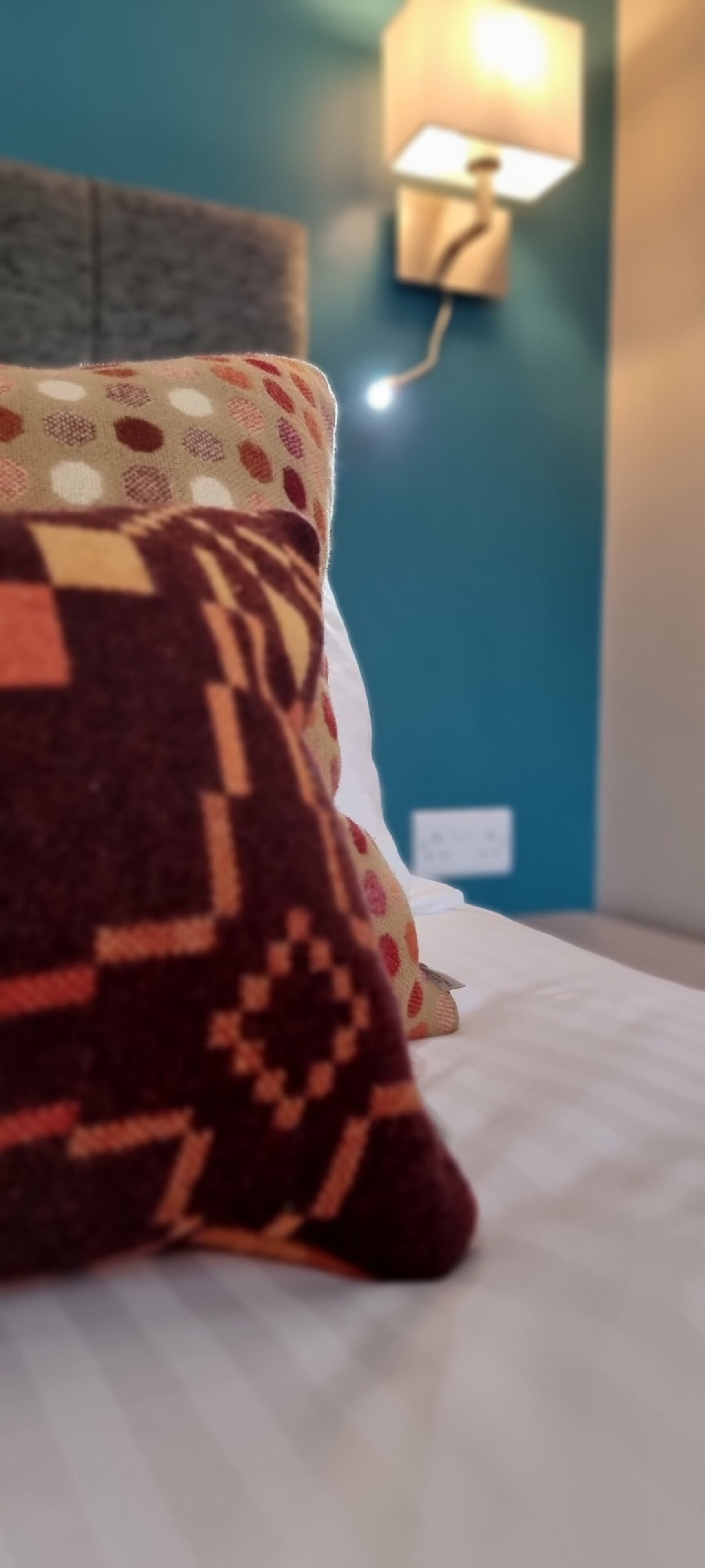 Una cama con una almohada estampada y una lámpara fijada a la pared.