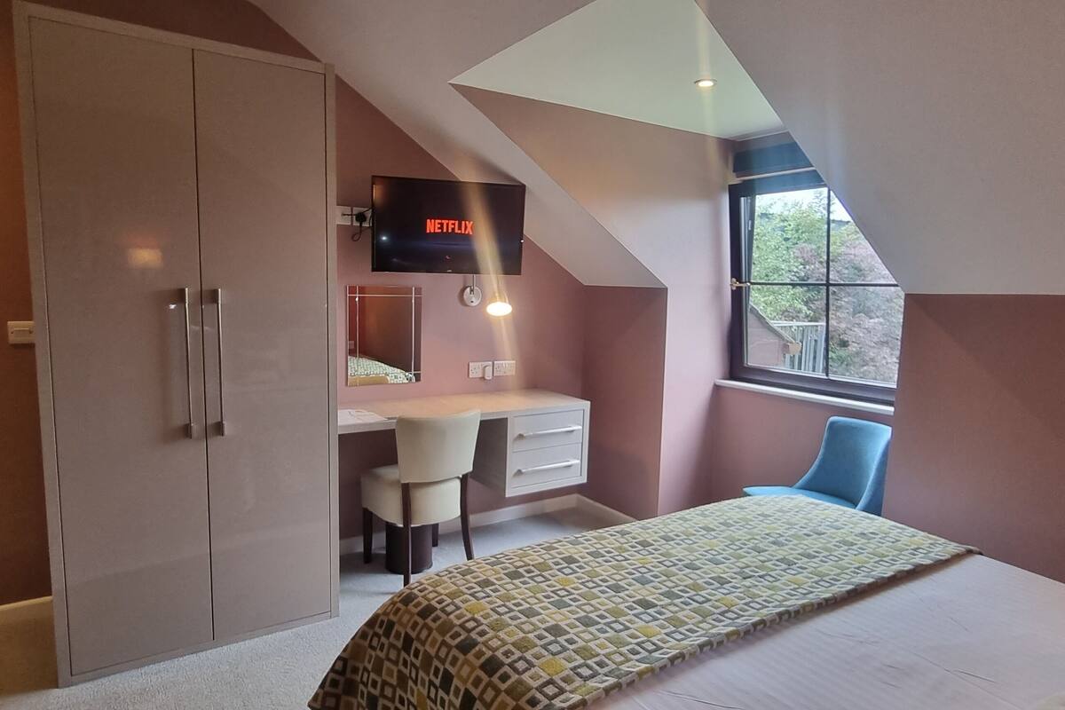 A bedroom with a bed, a desk, a chair, and a TV displaying Netflix.