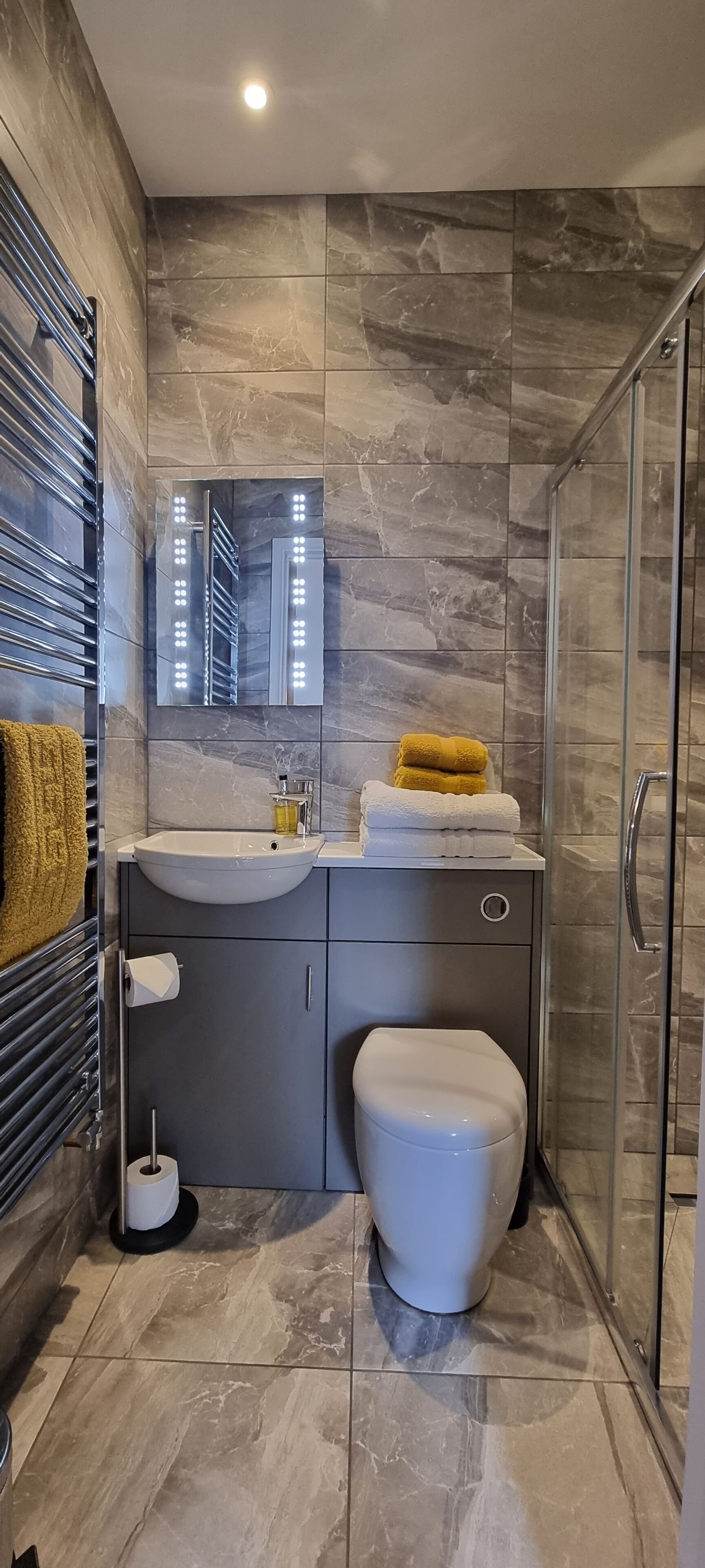 A modern bathroom with a glass shower enclosure, a white toilet, a sink with a mirror above it, and a towel rack with towels.