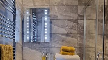 A modern bathroom with a glass shower enclosure, a white toilet, a sink with a mirror above it, and a towel rack with towels.