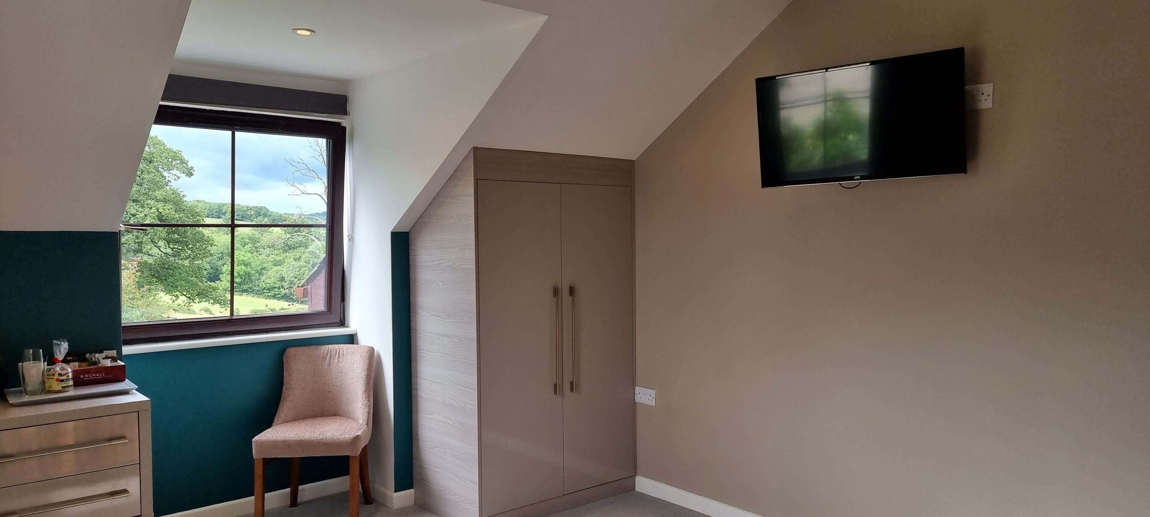 Ein Zimmer mit großem Fenster, einem an der Wand befestigten Fernseher und einem Kleiderschrank.