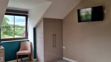 A room with a large window, a television mounted on the wall, and a wardrobe.