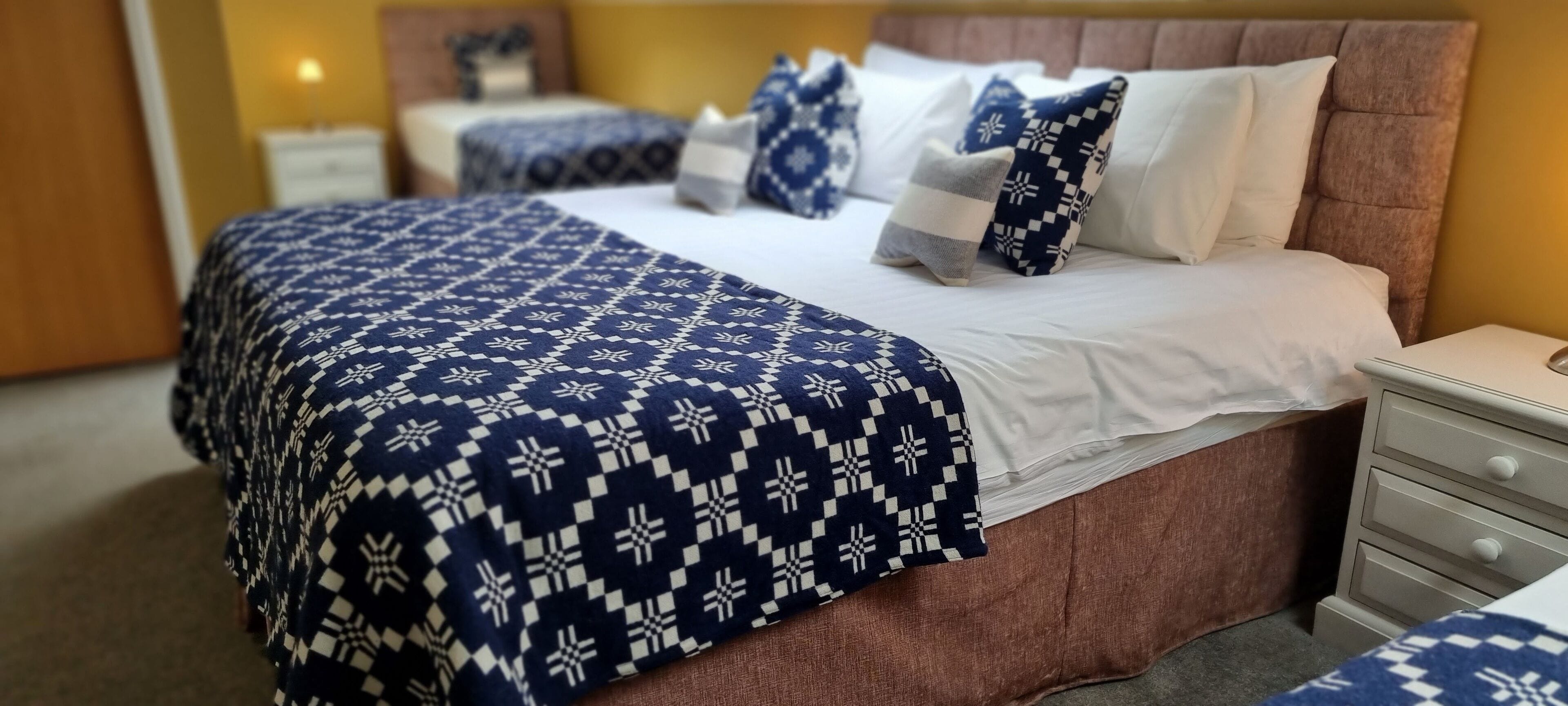 Un lit bien fait, avec une couvre-lit à motifs et des oreillers, une tête de lit en bois et une table de chevet dotée de tiroirs.