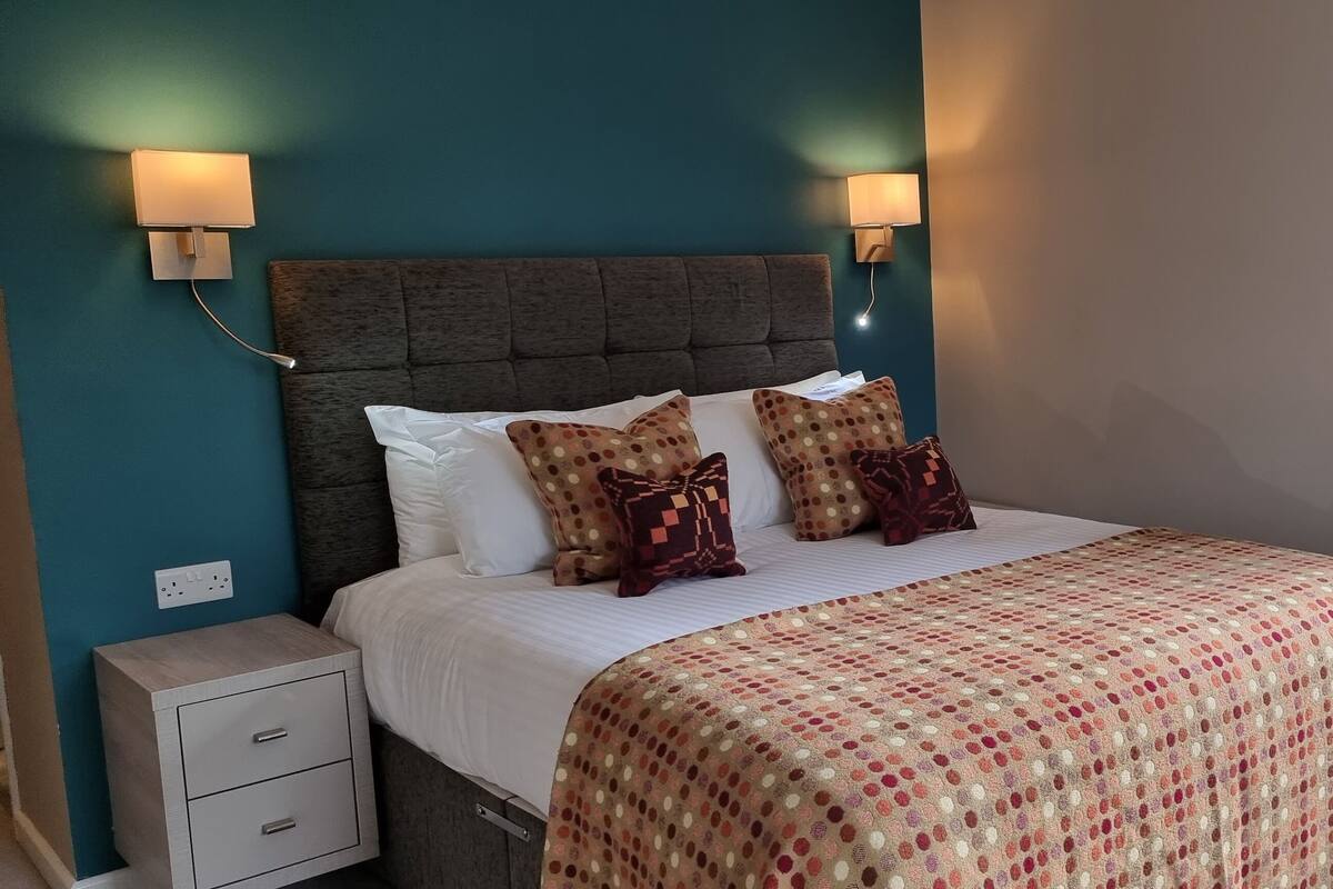 A bedroom with a bed, two wall-mounted lamps, a nightstand, and a window with curtains.