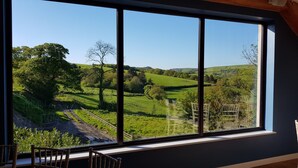 A room with a large window offering a view of a green landscape with hills and trees. - Llety Cynin (Carmarthen)