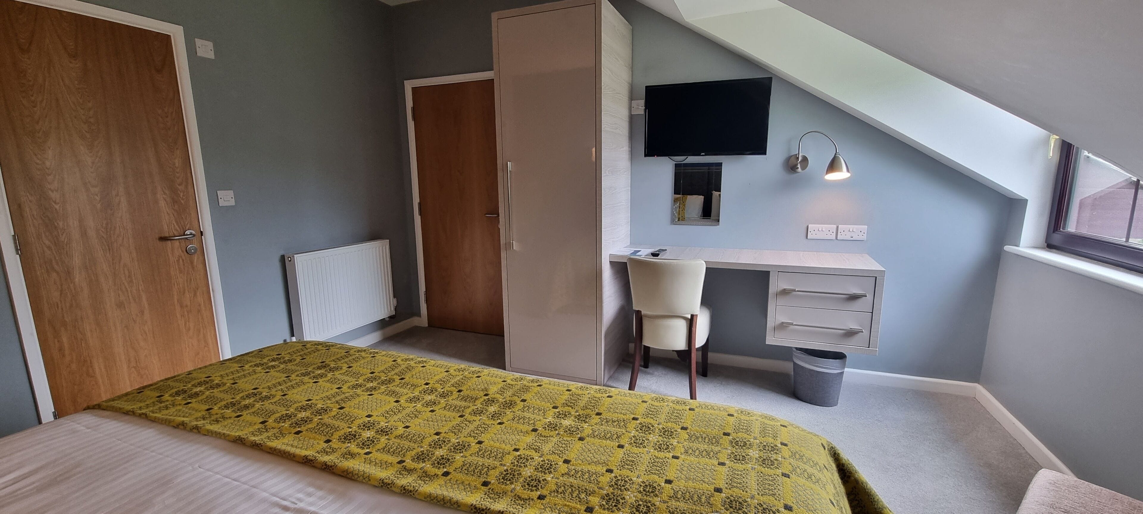 Une chambre à coucher avec un lit, un bureau, une chaise, une télévision et une fenêtre.