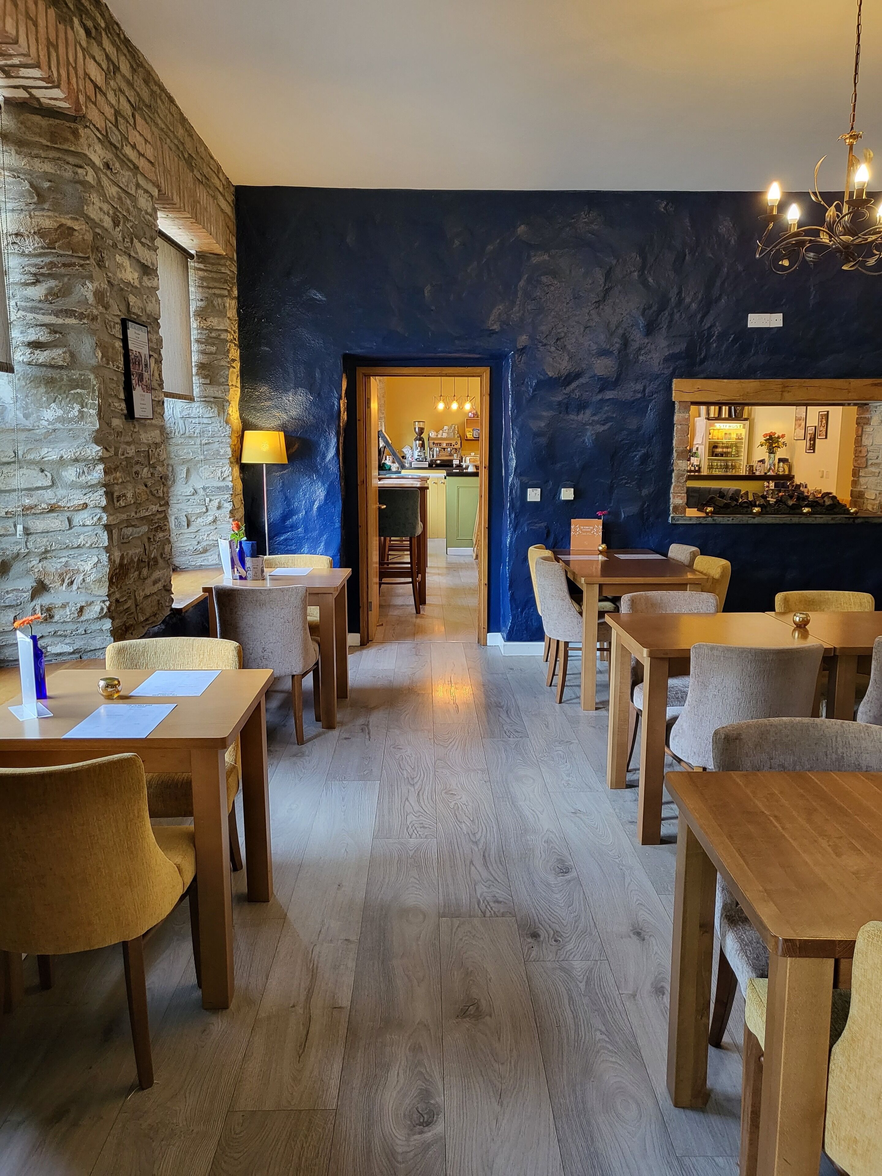 A cozy restaurant with wooden tables and chairs, a stone wall, and a blue accent wall.