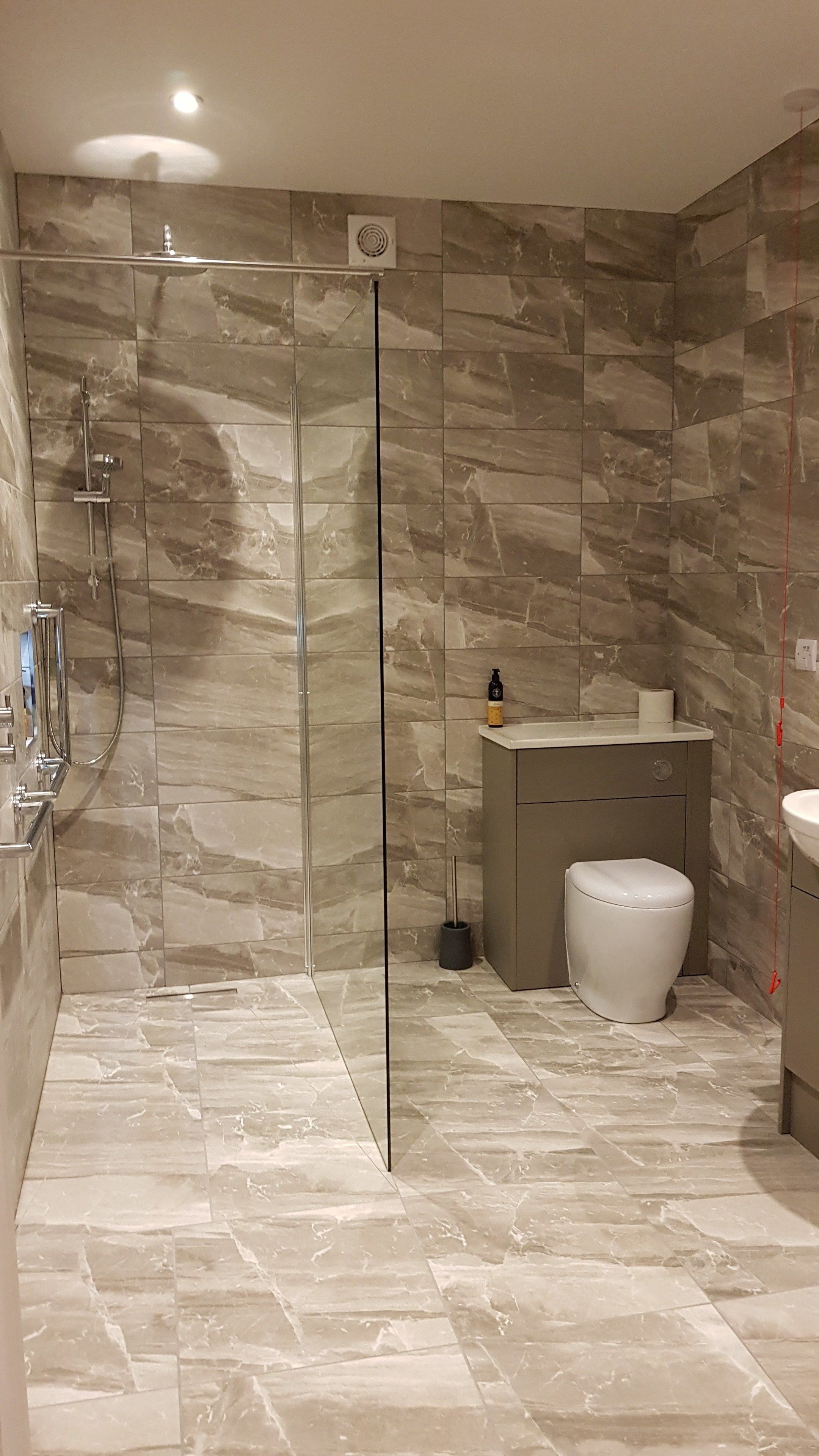 A modern bathroom with a glass-enclosed shower, marble flooring, and a toilet.
