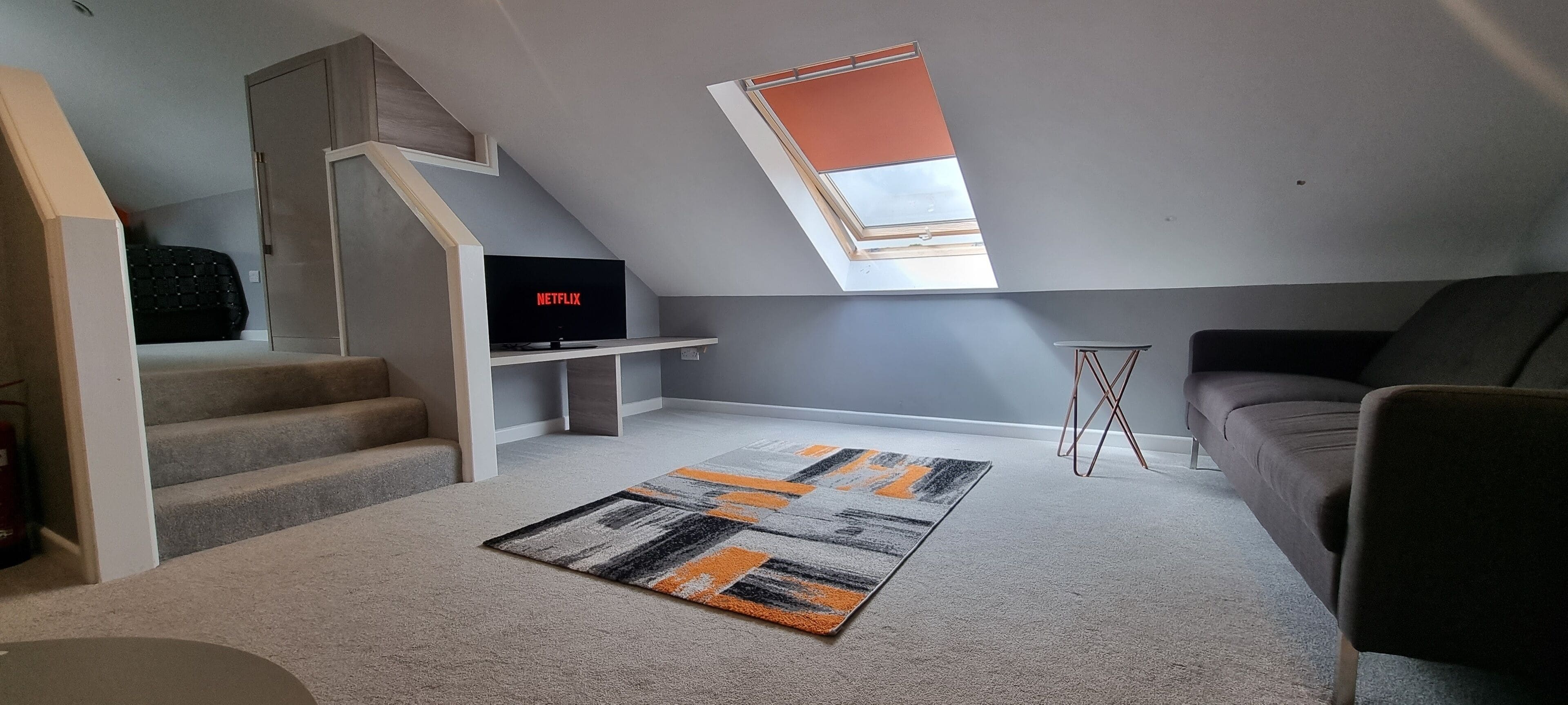 Um apartamento loft moderno com escada, televisão de tela plana em um suporte, sofá e tapete estampado.