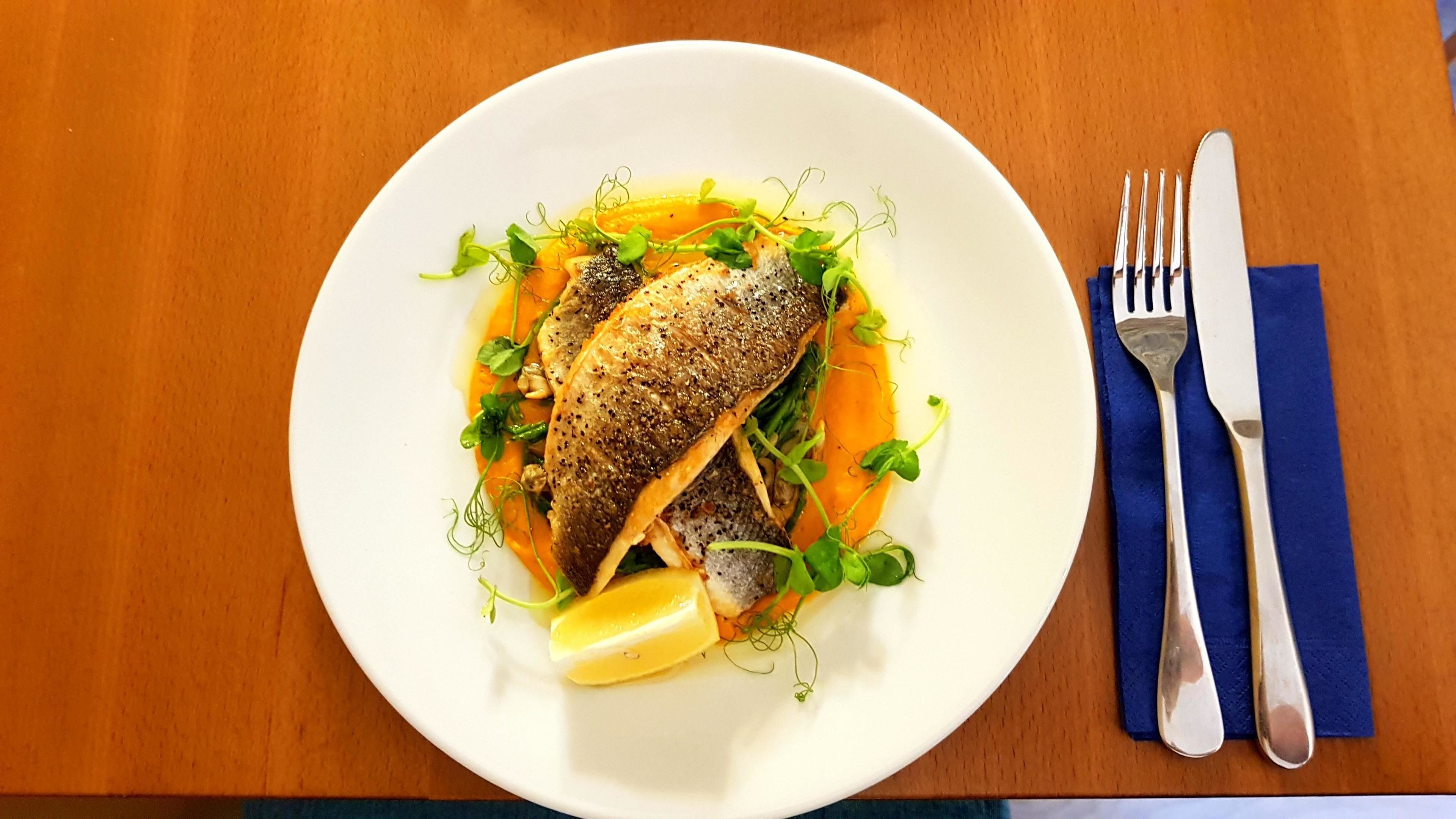 Ein weißer Teller mit Fisch, Zitrone und grünem Gemüse auf einer Holztischplatte.