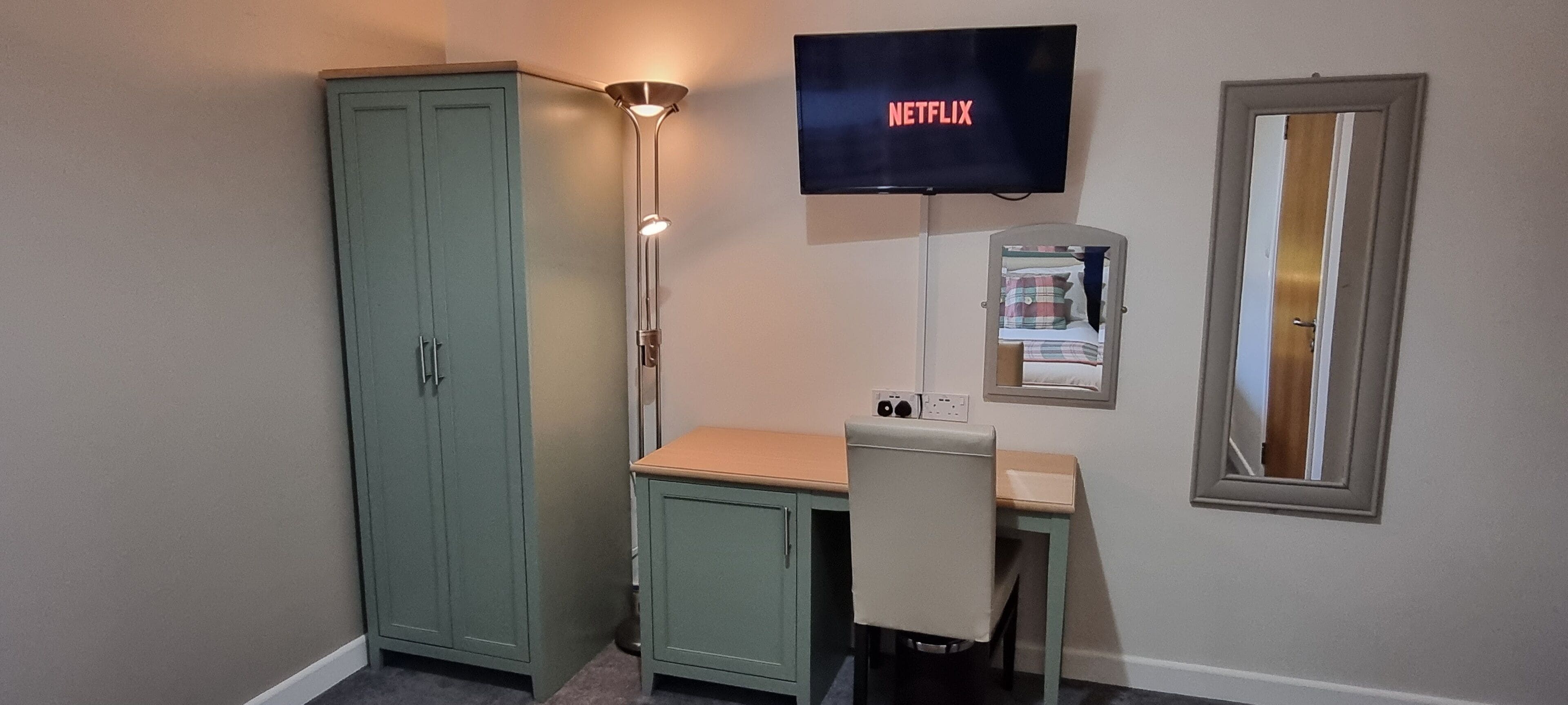 A room with a desk, a cabinet, a television displaying 'NETFLIX', and a mirror.