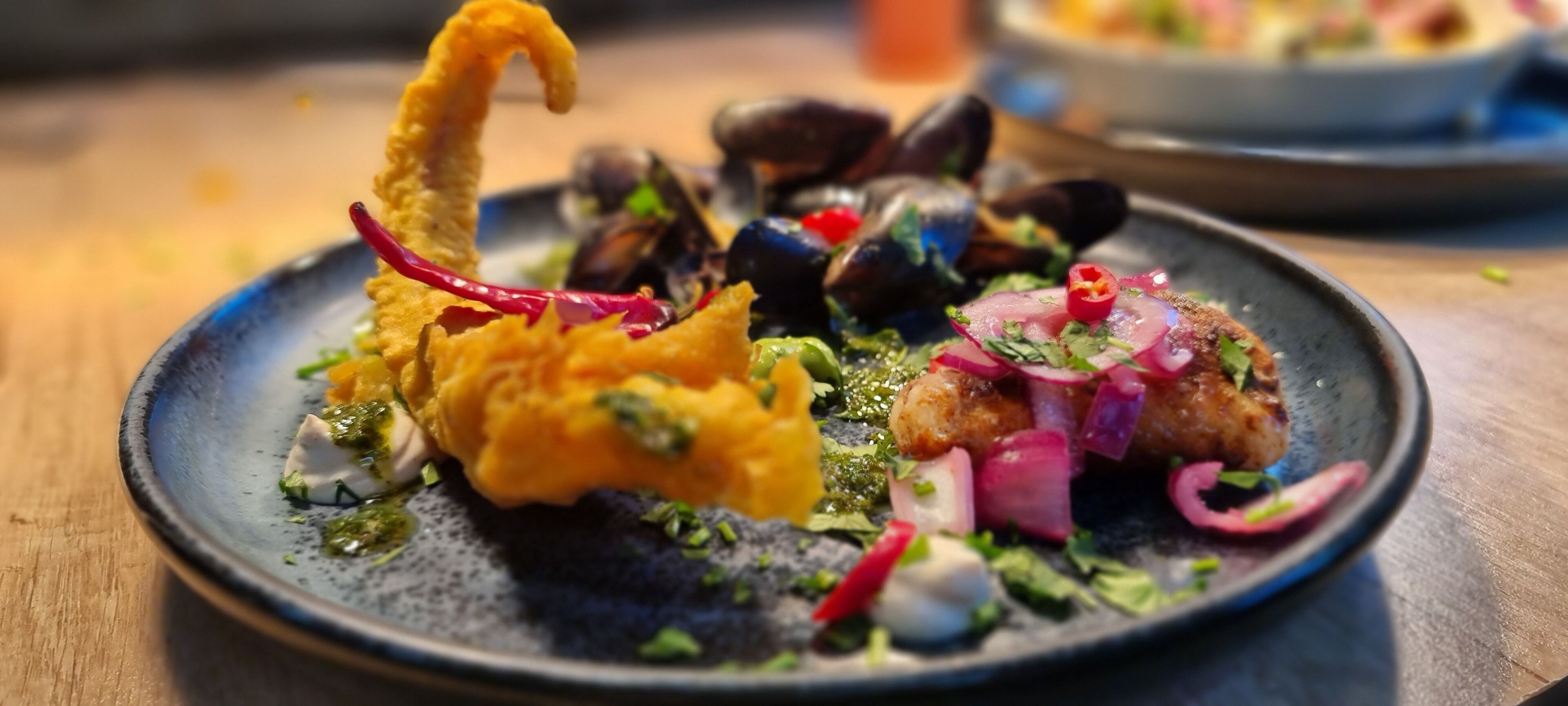 A plate of food with mussels, a fried item, and a salad with red onions and herbs.