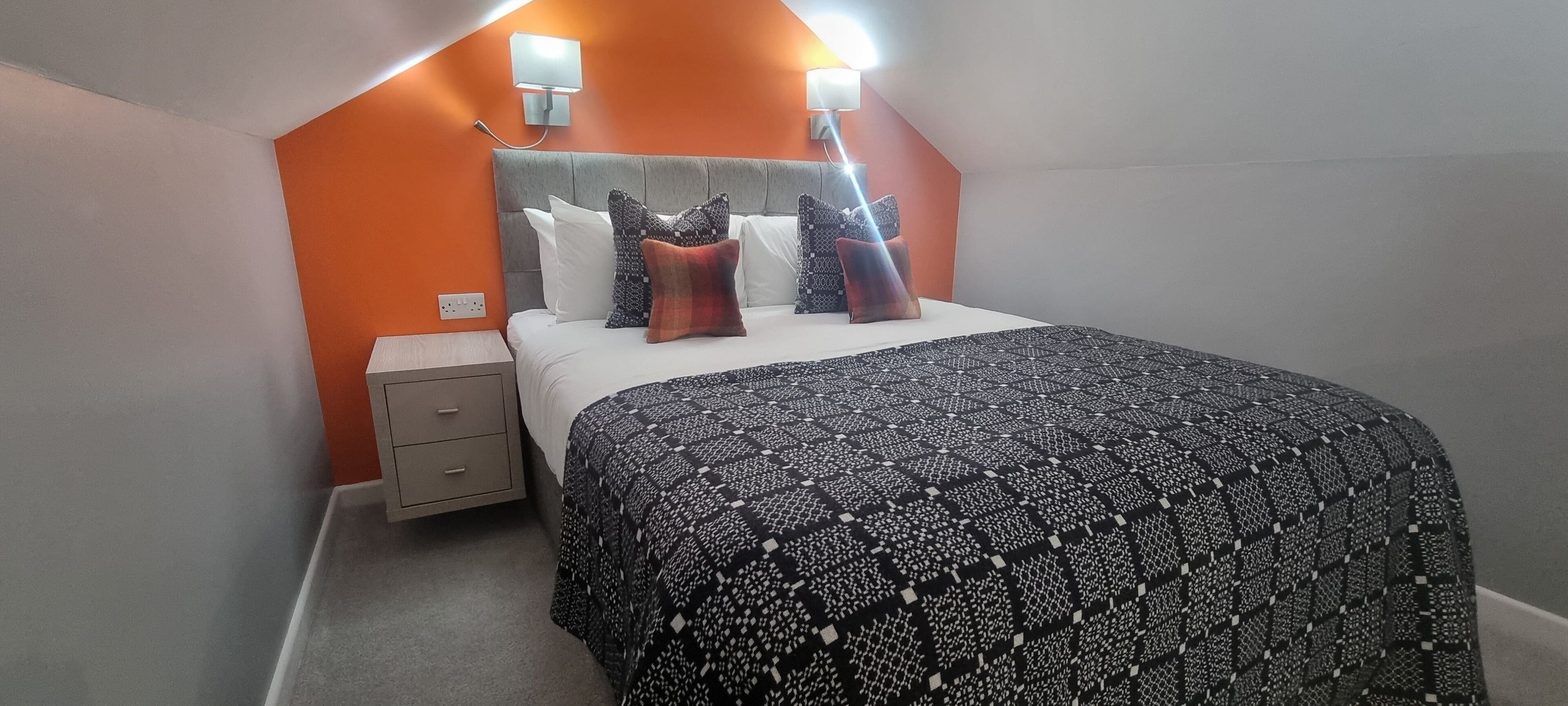Un dormitorio con cama, mesita de noche y dos lámparas fijadas a la pared.