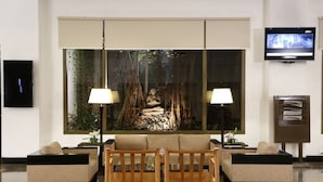 A lobby with a sofa, two chairs, a television, and a large window with a view of trees.