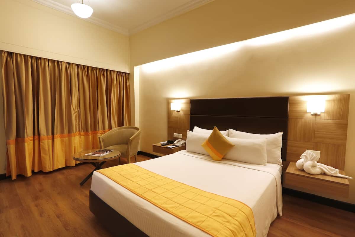 A hotel room with a large bed, a bedside table, a chair, a small table, and curtains.