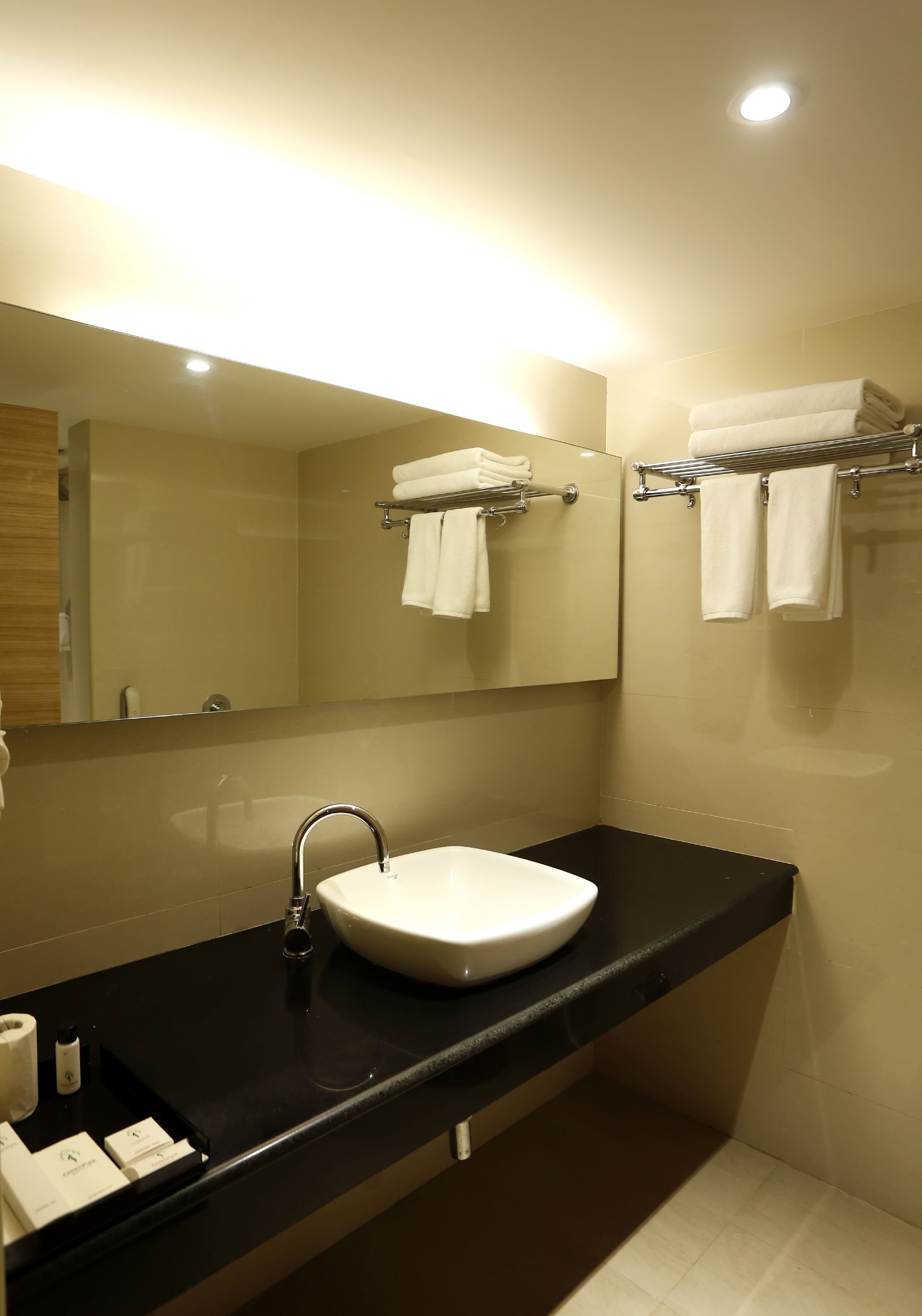 Une salle de bain moderne avec un lavabo blanc, un plan de toilette noir et un miroir au-dessus du lavabo. Des serviettes sont suspendues sur un porte-serviettes placé au-dessus du miroir.