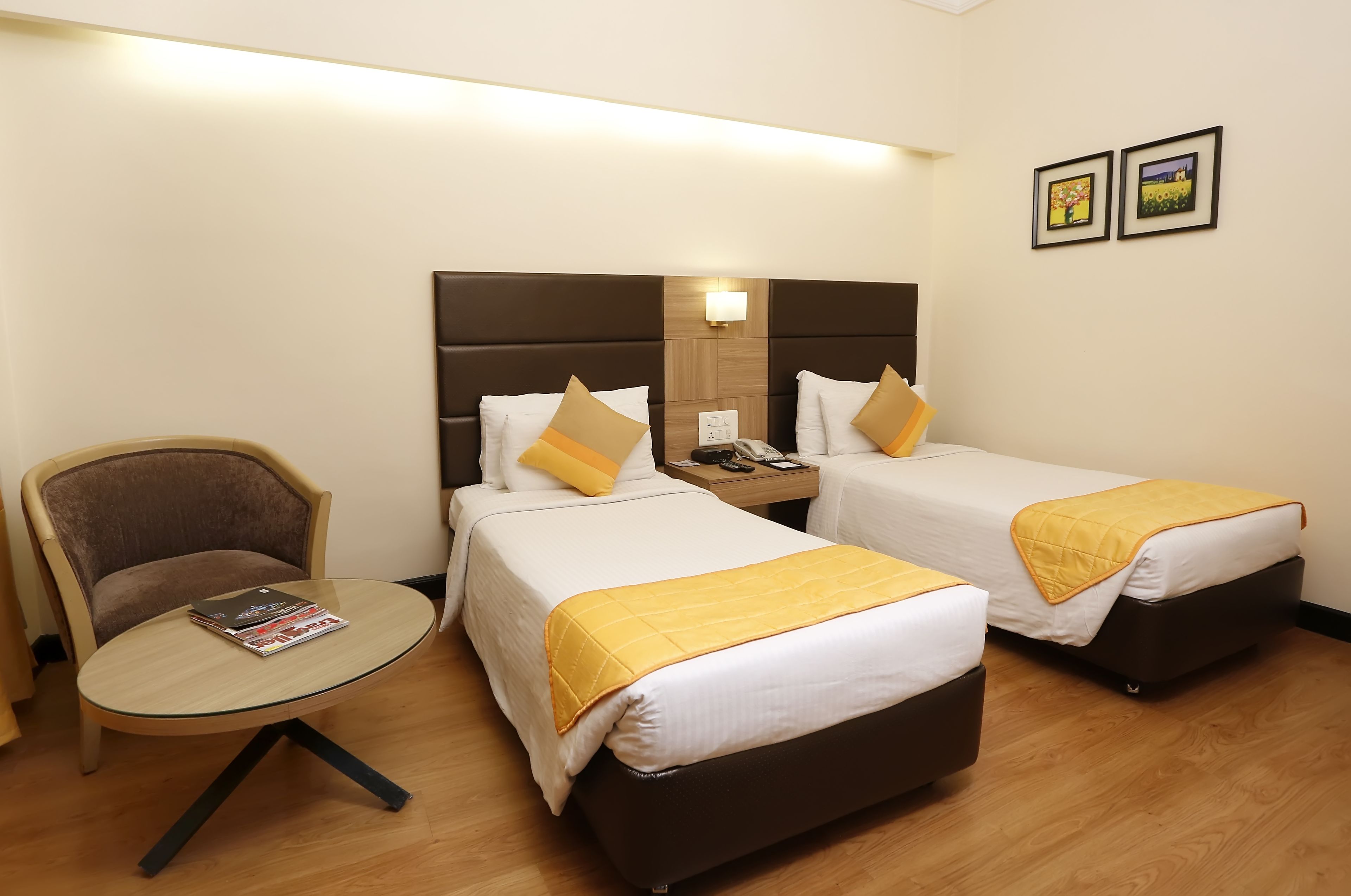 A hotel room with two single beds, a small round table, a chair, and a nightstand.