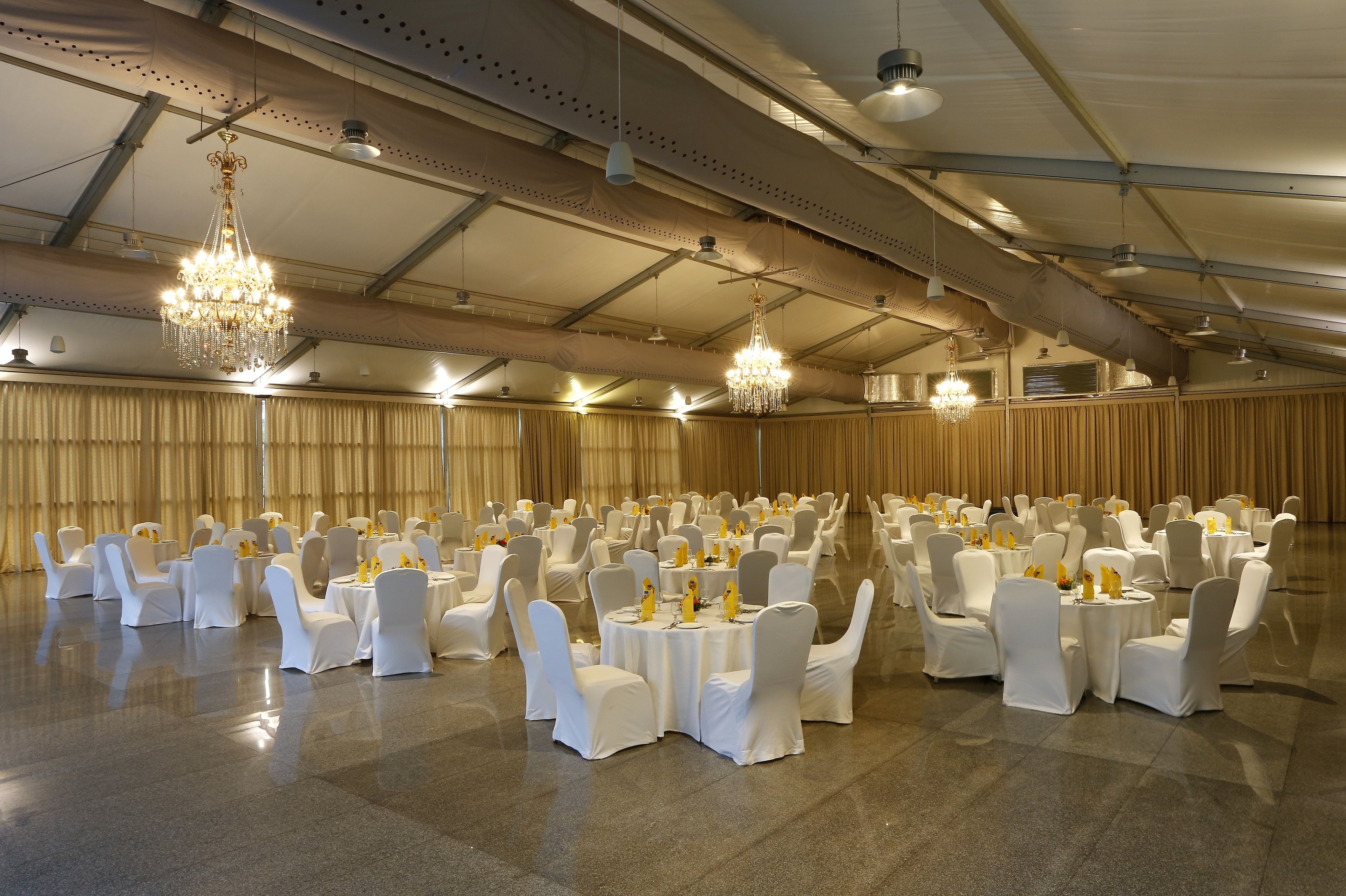 Een balzaal met ronde tafels en witte stoelen, lustra en een hoge plafond.