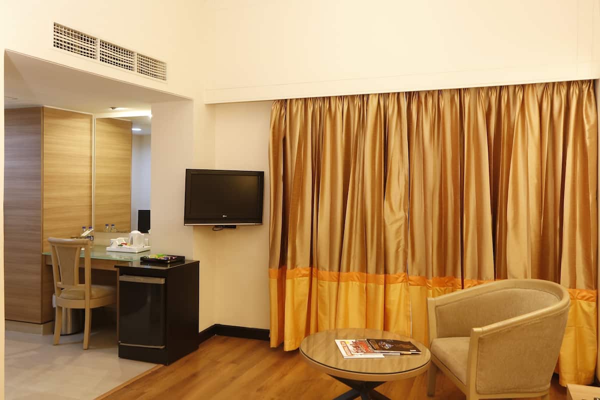 A hotel room with a dining area, a TV, a sofa, and a curtain.