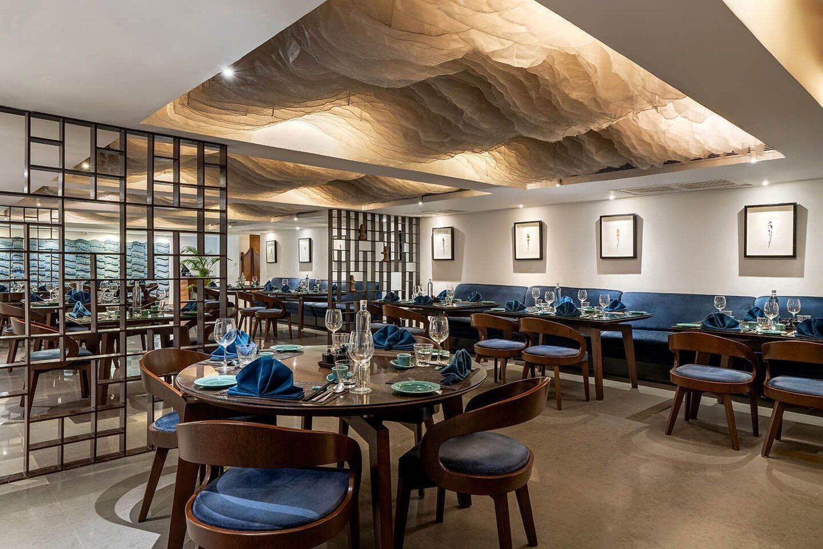 A restaurant with round tables, blue upholstered chairs, and a modern ceiling design.
